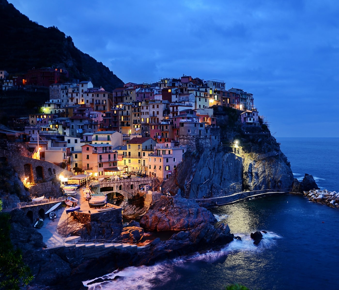 Manarola zur blauen Stunde: die farbigen Turmhäuser stapeln sich über der Bootsrampe die Steilküste hinauf, die Fenster leuchten warm